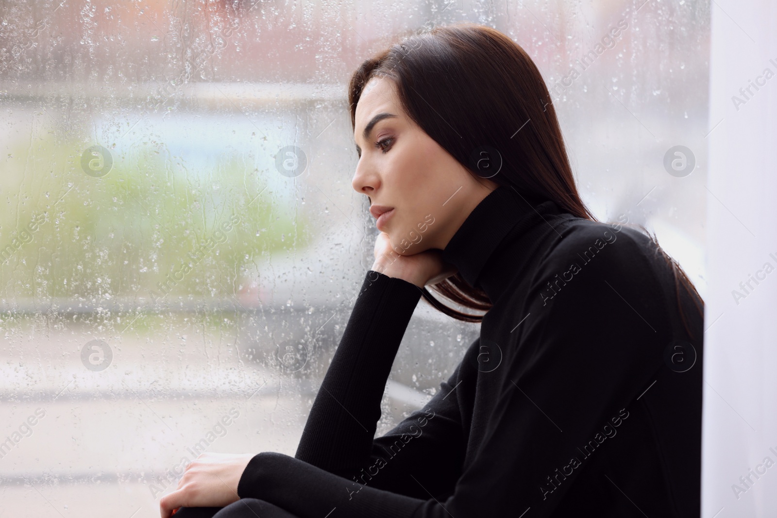 Photo of Depressed woman near window on rainy day, space for text