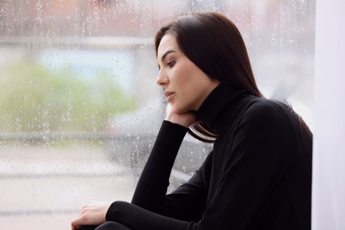 Depressed woman near window on rainy day, space for text