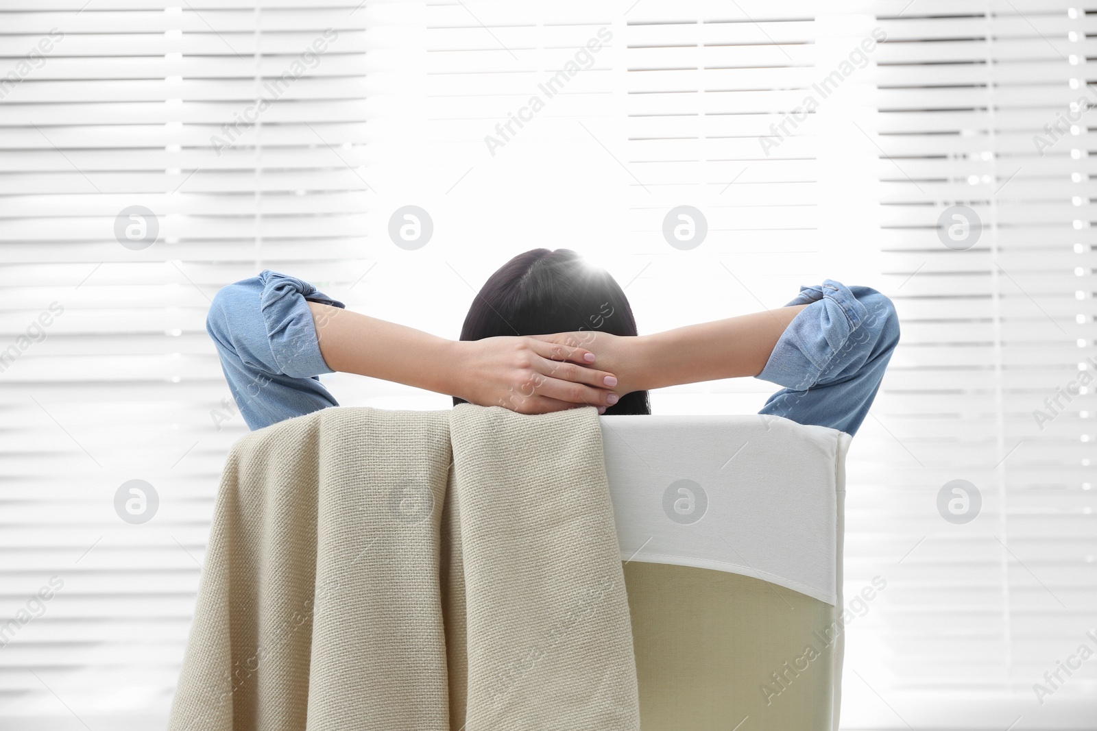 Photo of Young woman relaxing in armchair near window at home, back view