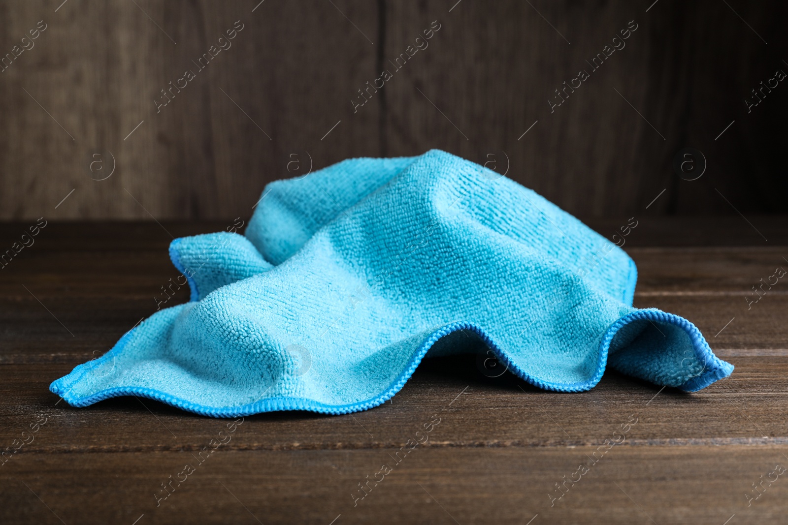 Photo of Light blue microfiber cloth on wooden table, closeup