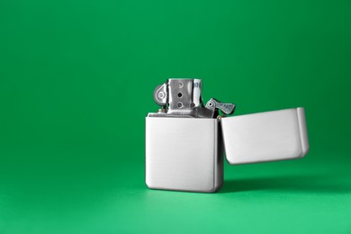 Gray metallic cigarette lighter on green background, space for text