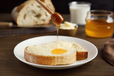 Photo of Pouring honey from dipper onto sandwich with butter on wooden table, closeup