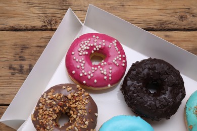 Photo of Box with different tasty glazed donuts on wooden table, closeup