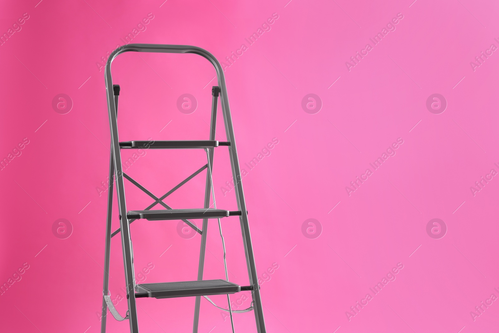 Photo of Modern metal stepladder on pink background. Space for text