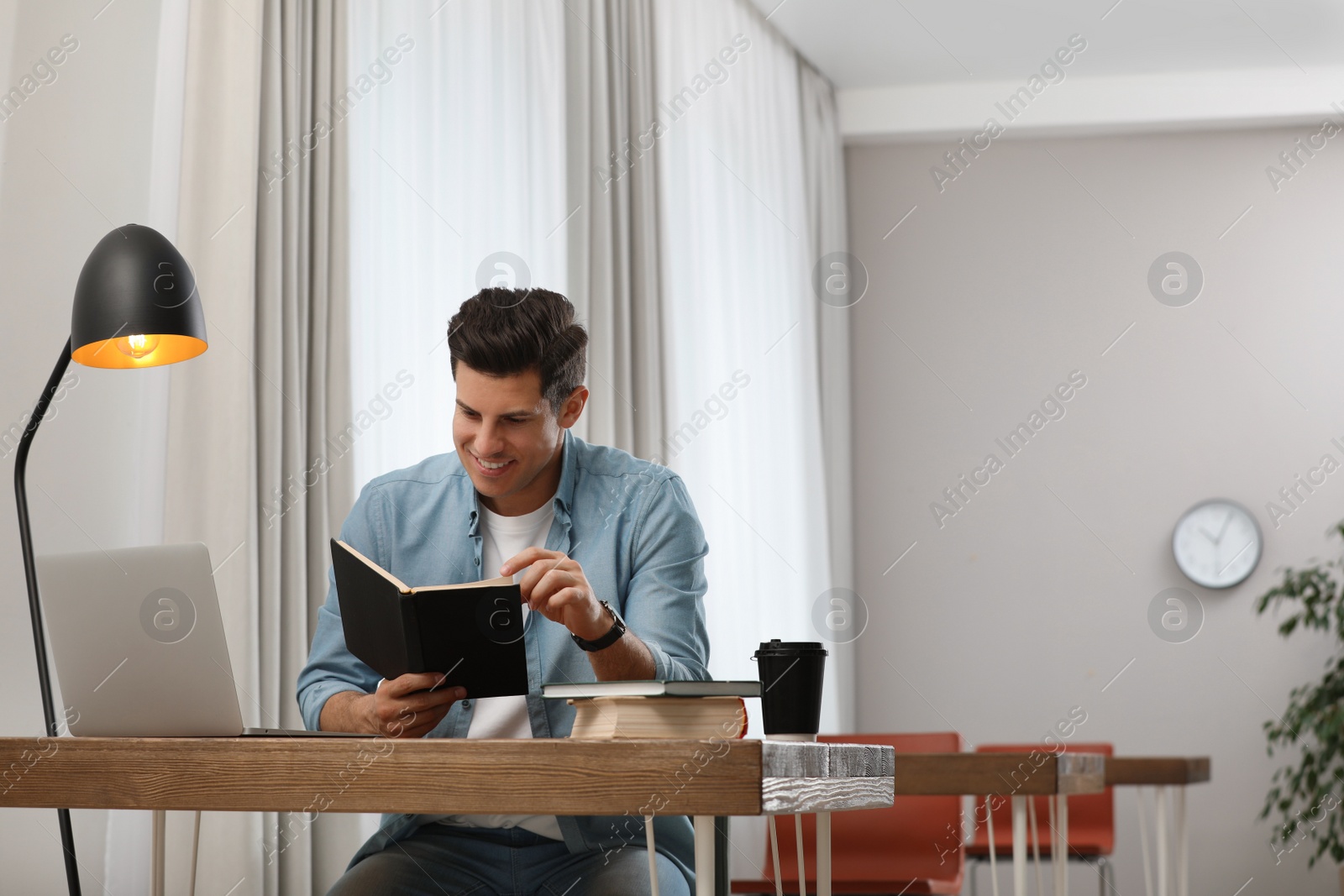 Photo of Man reading book at table in library