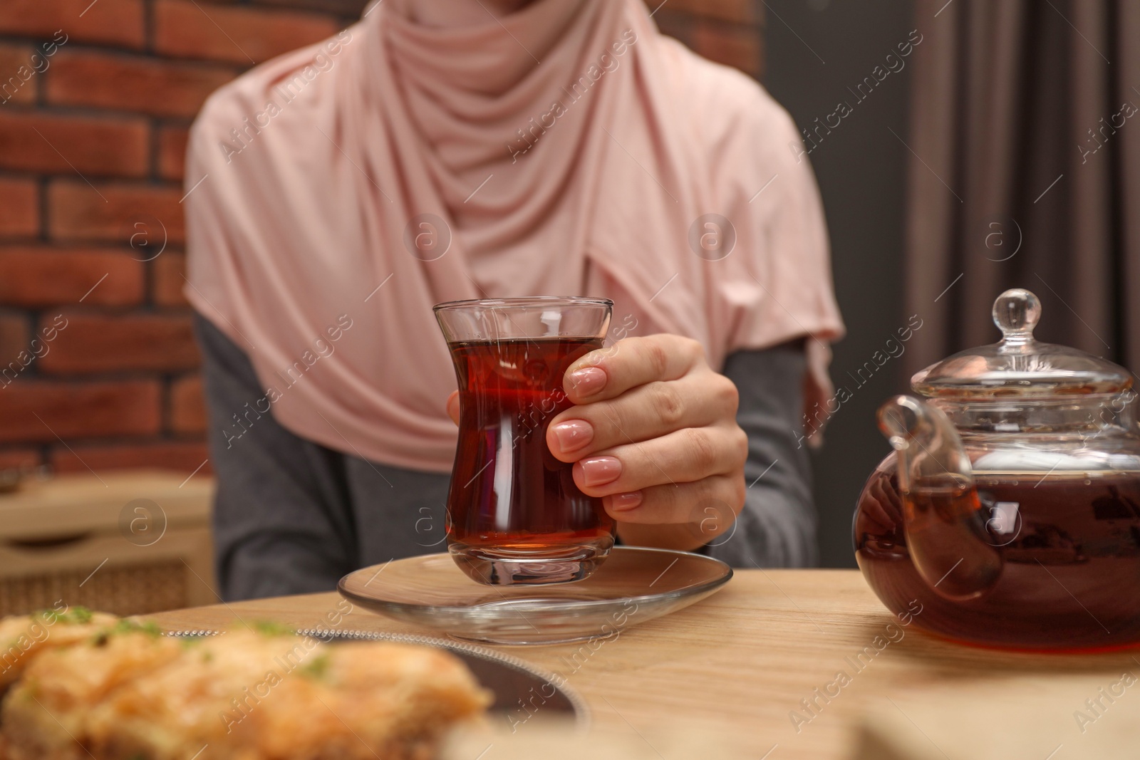 Photo of Woman with cup of delicious Turkish tea at wooden table, closeup