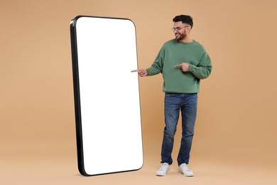 Image of Man pointing at huge mobile phone with empty screen on dark beige background. Mockup for design