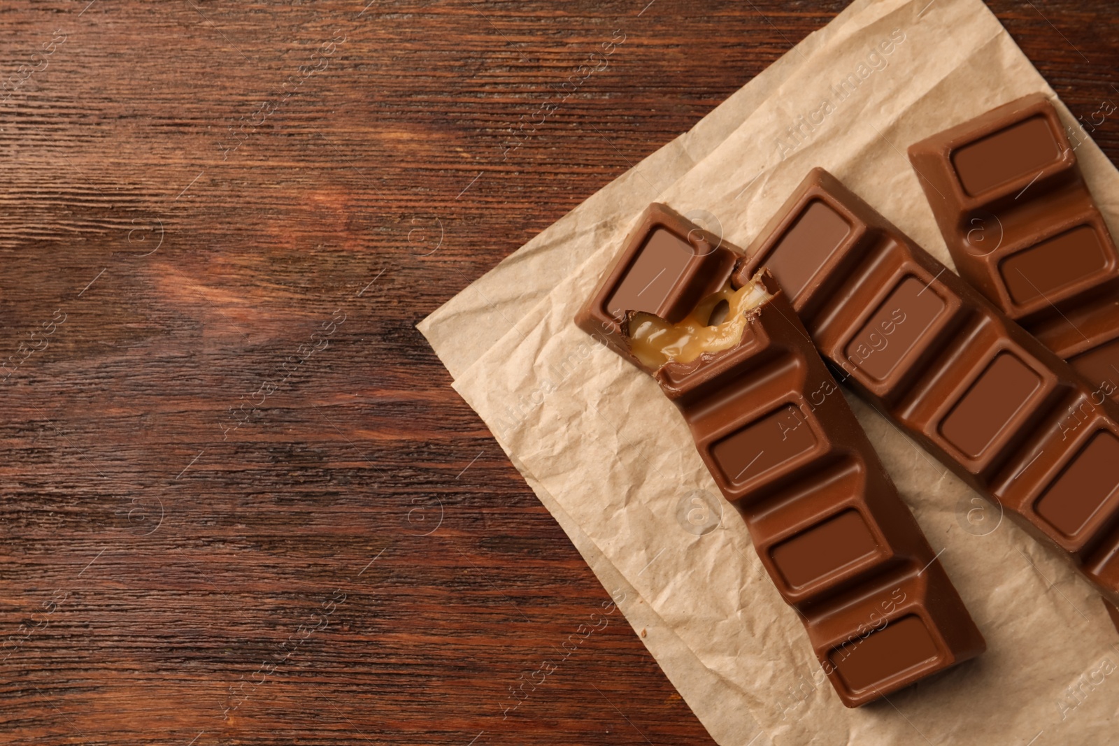 Photo of Tasty chocolate bars on wooden table, top view. Space for text