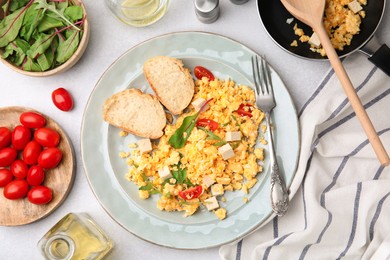 Photo of Delicious scrambled eggs with tofu and slices of baguettes served on light grey table, flat lay