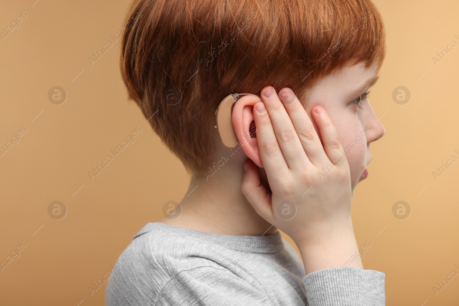 Photo of Little boy with hearing aid on pale brown background