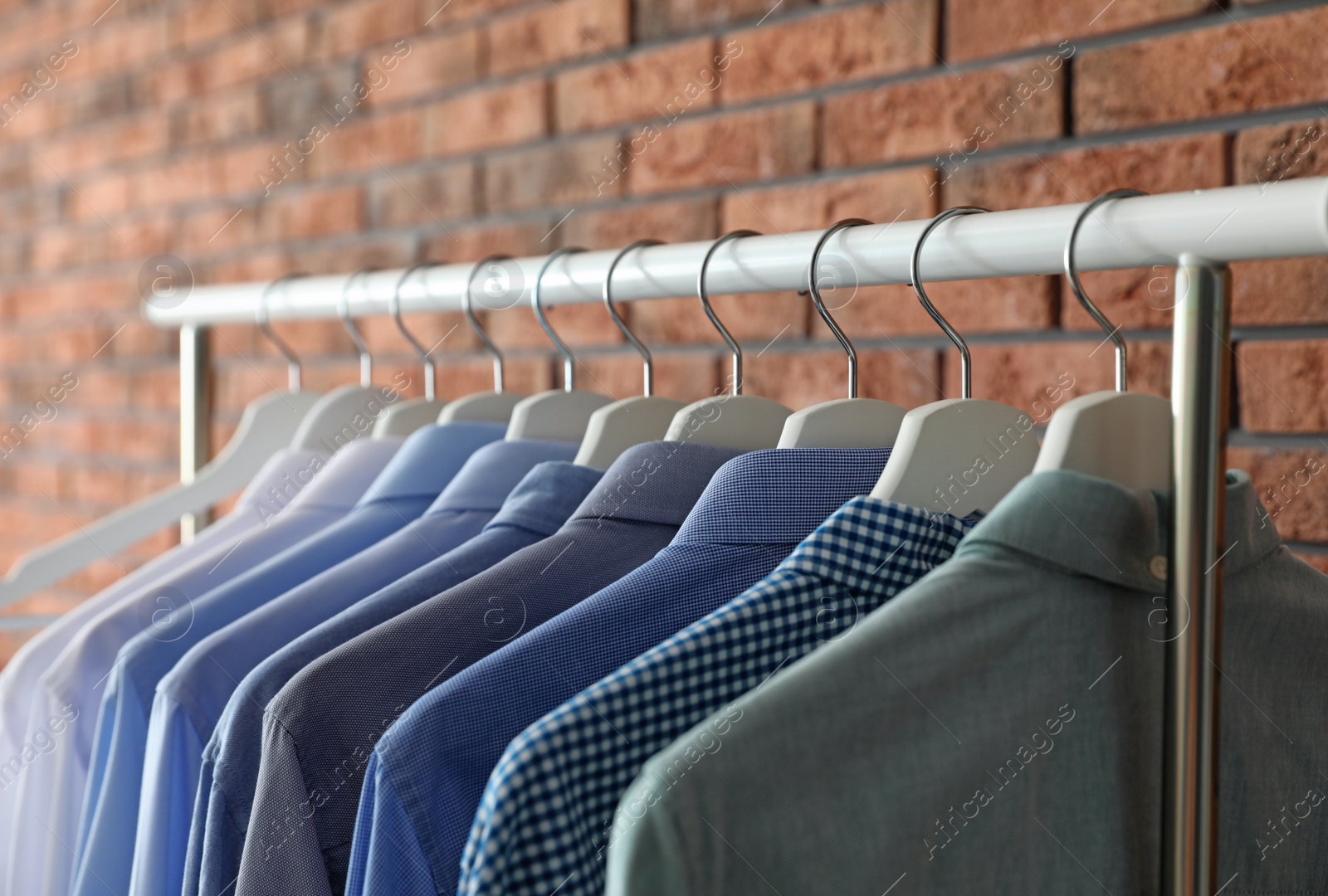 Photo of Wardrobe rack with men's clothes near brick wall, closeup