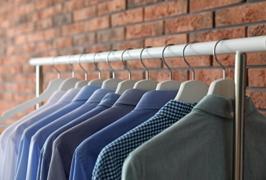 Photo of Wardrobe rack with men's clothes near brick wall, closeup