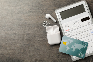 Photo of Credit card, calculator and wireless earphones on grey table, flat lay. Space for text