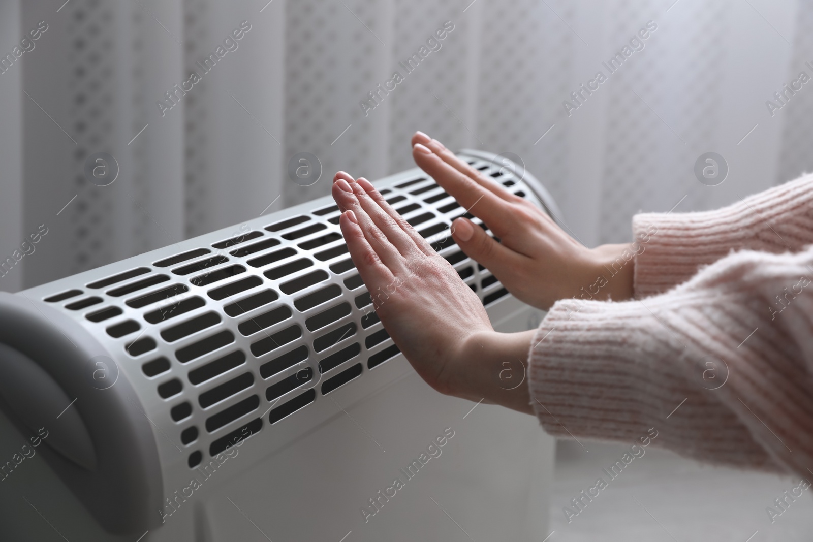 Photo of Woman warming hands near electric heater at home, closeup