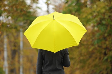 Woman with yellow umbrella in autumn park, back view