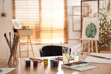 Photo of Paints and brushes on wooden table in art studio