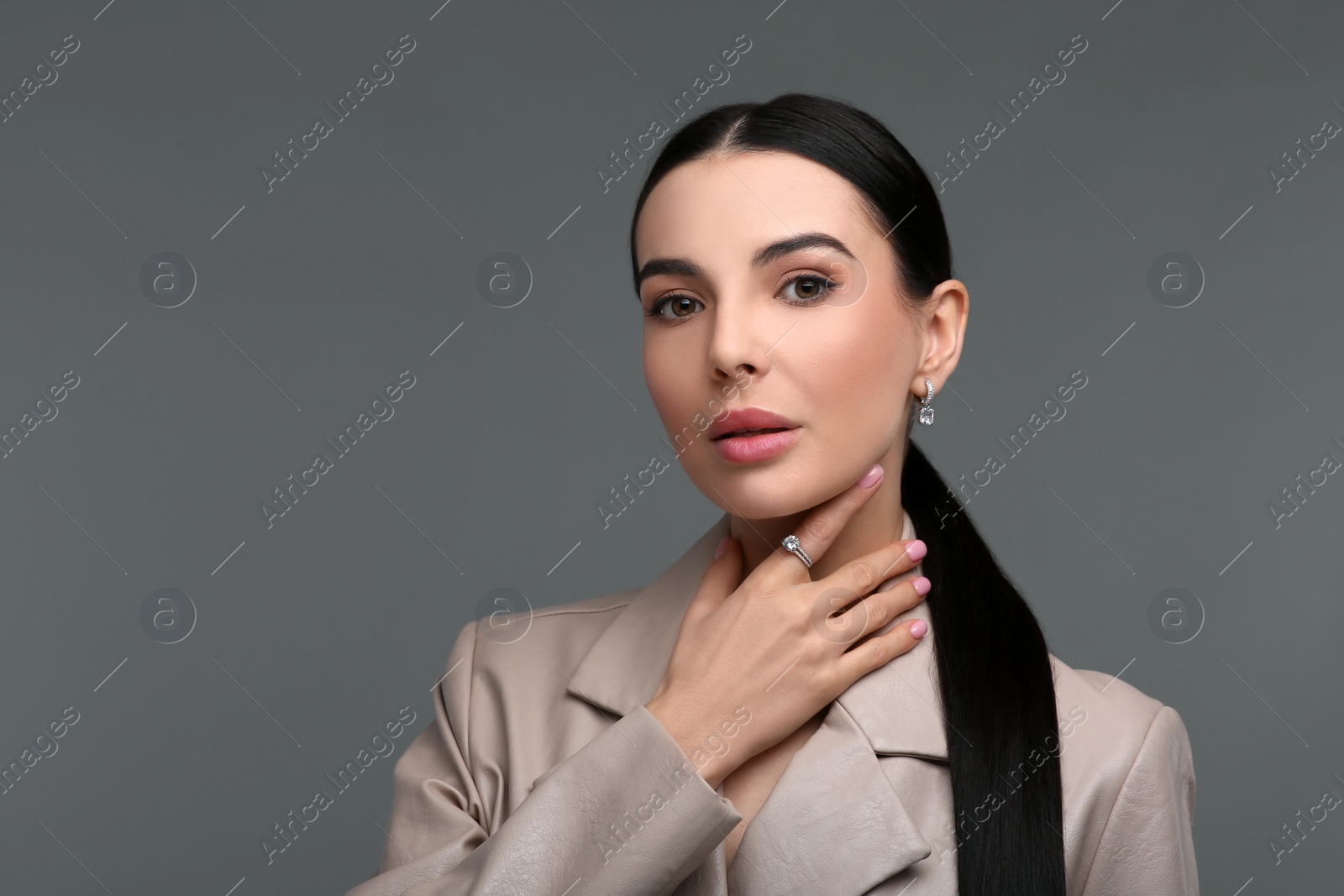 Photo of Beautiful young woman with elegant jewelry on dark grey background