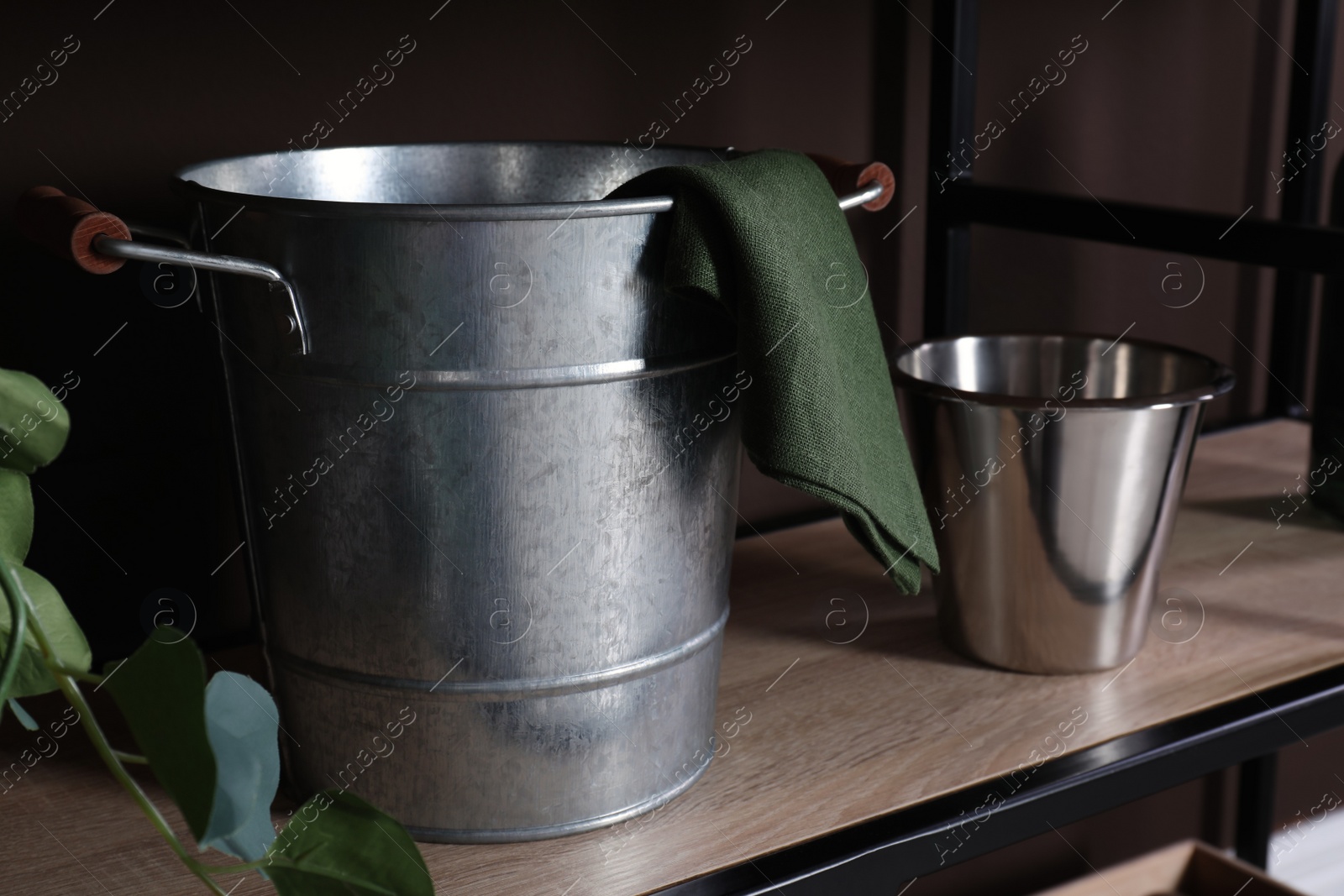 Photo of Metal buckets and napkin on wooden shelf near brown wall