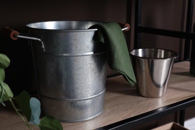 Metal buckets and napkin on wooden shelf near brown wall