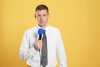 Male journalist with microphone on yellow background