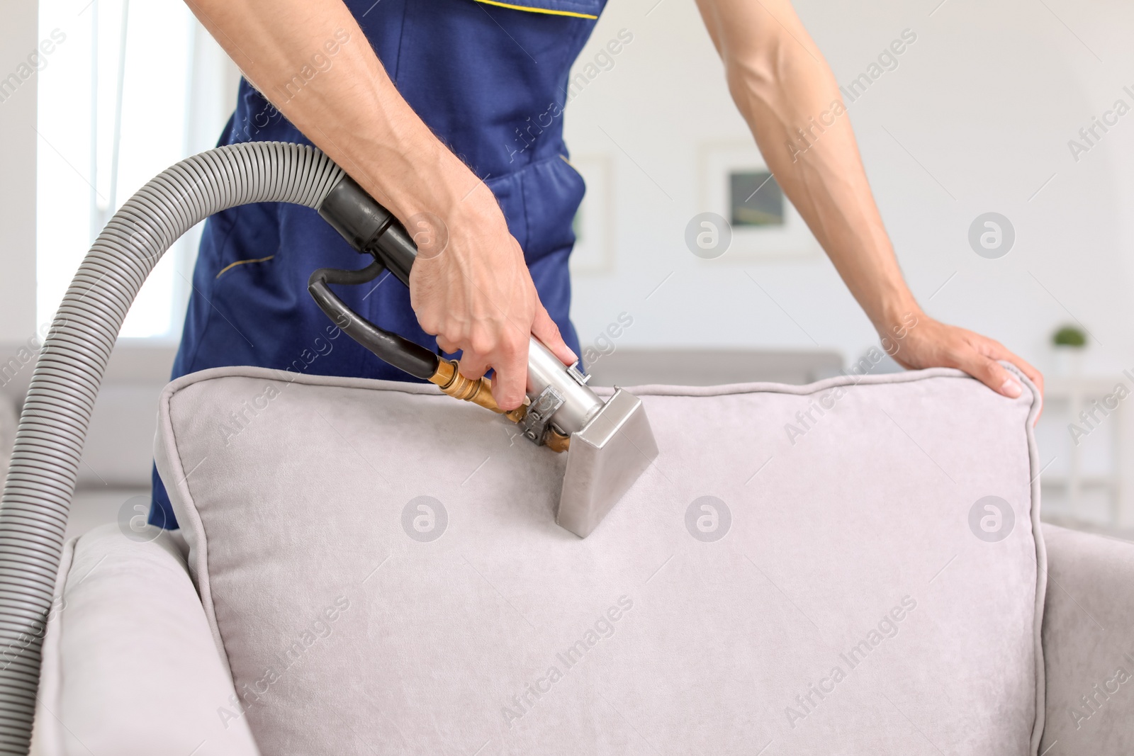 Photo of Dry cleaning worker removing dirt from armchair indoors