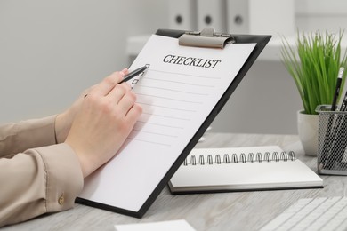 Photo of Woman filling Checklist at white wooden table indoors, closeup