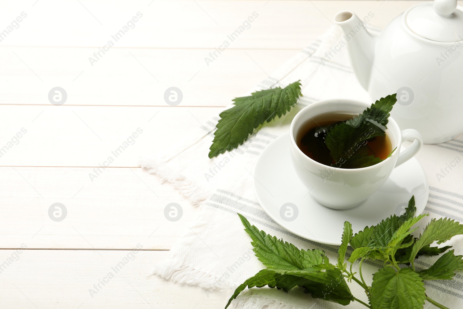 Photo of Aromatic nettle tea and green leaves on white wooden table, space for text