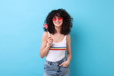 Beautiful woman in sunglasses with lollipop on light blue background