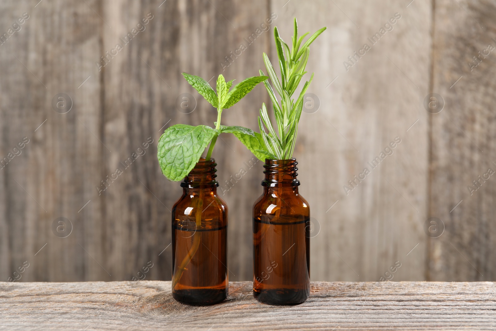 Photo of Bottles with essential oils, mint and rosemary on wooden table
