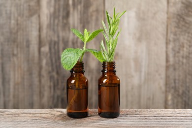 Photo of Bottles with essential oils, mint and rosemary on wooden table