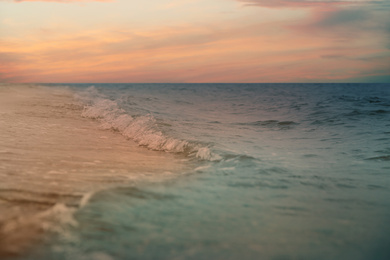 Image of Ocean waves rolling on sandy beach under sky with clouds at sunset, closeup