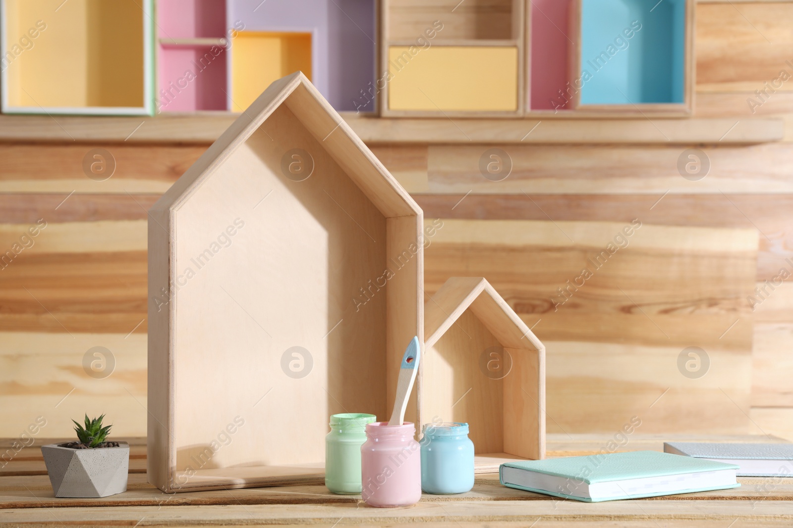 Photo of Composition with house shaped shelves and jars of paints on wooden table. Interior elements