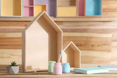 Photo of Composition with house shaped shelves and jars of paints on wooden table. Interior elements