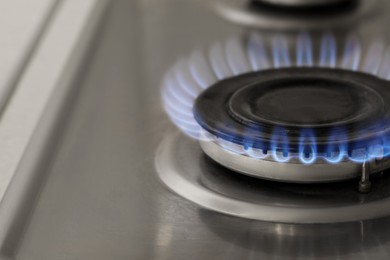 Photo of Gas burner with burning flame on cooktop, closeup