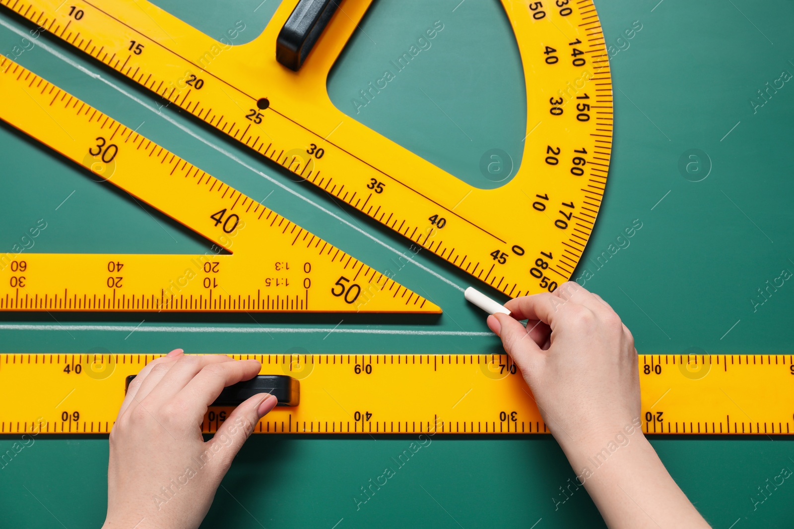 Photo of Woman drawing with chalk, ruler, triangle and protractor on green board, closeup