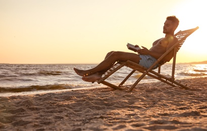 Photo of Young man reading book in deck chair on beach