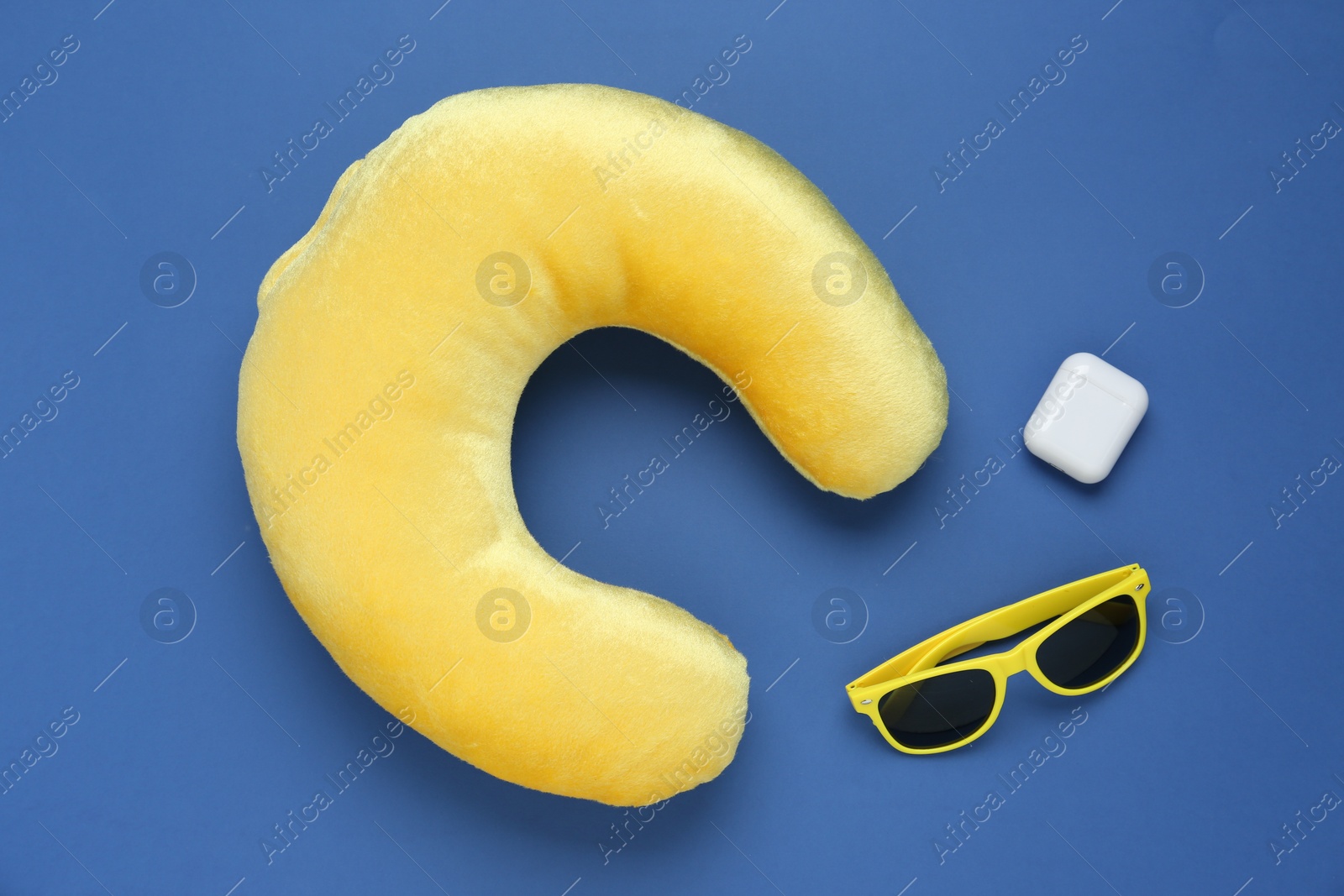 Photo of Yellow travel pillow, sunglasses and earphones on blue background, flat lay