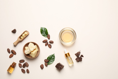 Organic cocoa butter, beans and essential oil on beige background, flat lay