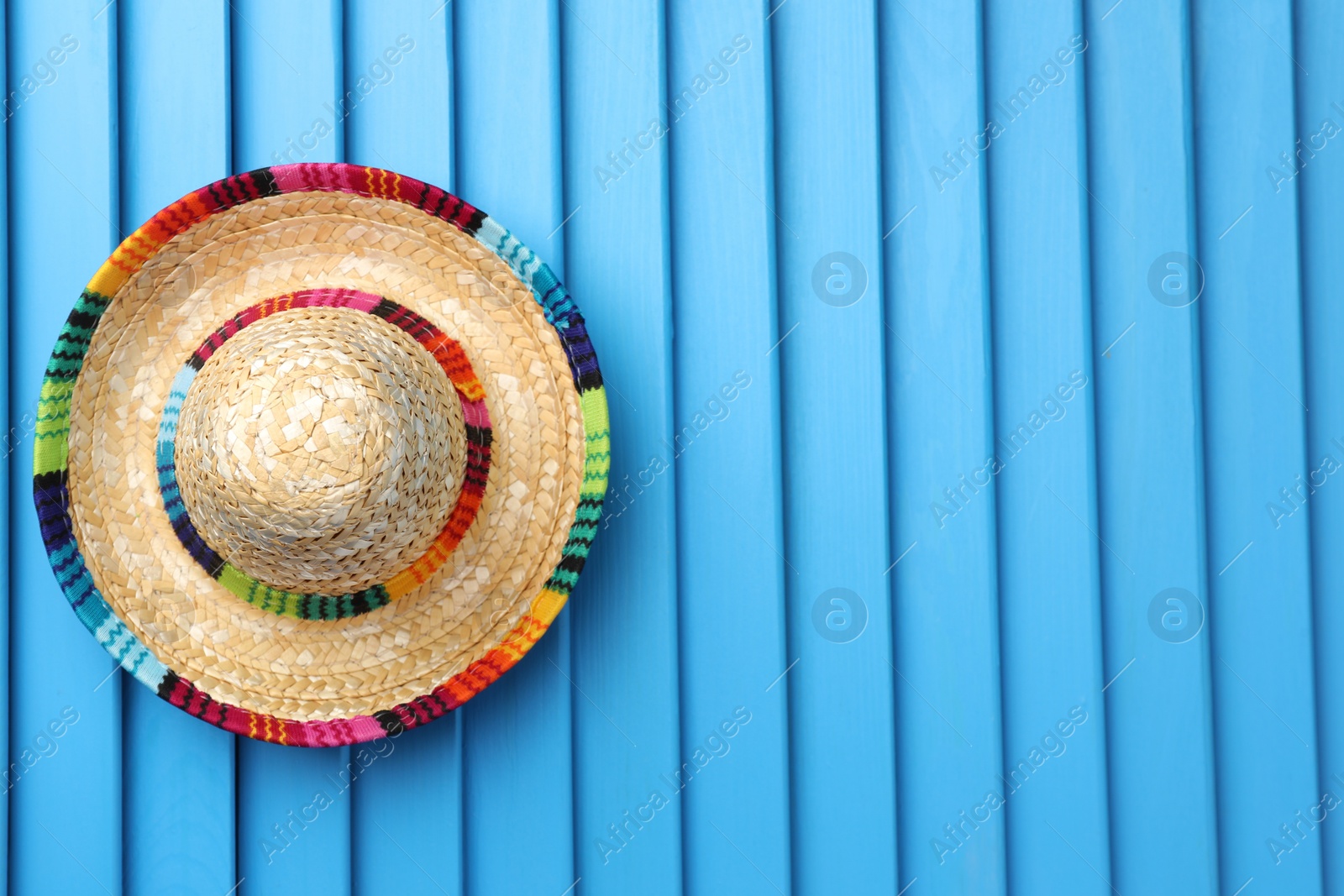Photo of Mexican sombrero hat on blue wooden surface, top view. Space for text