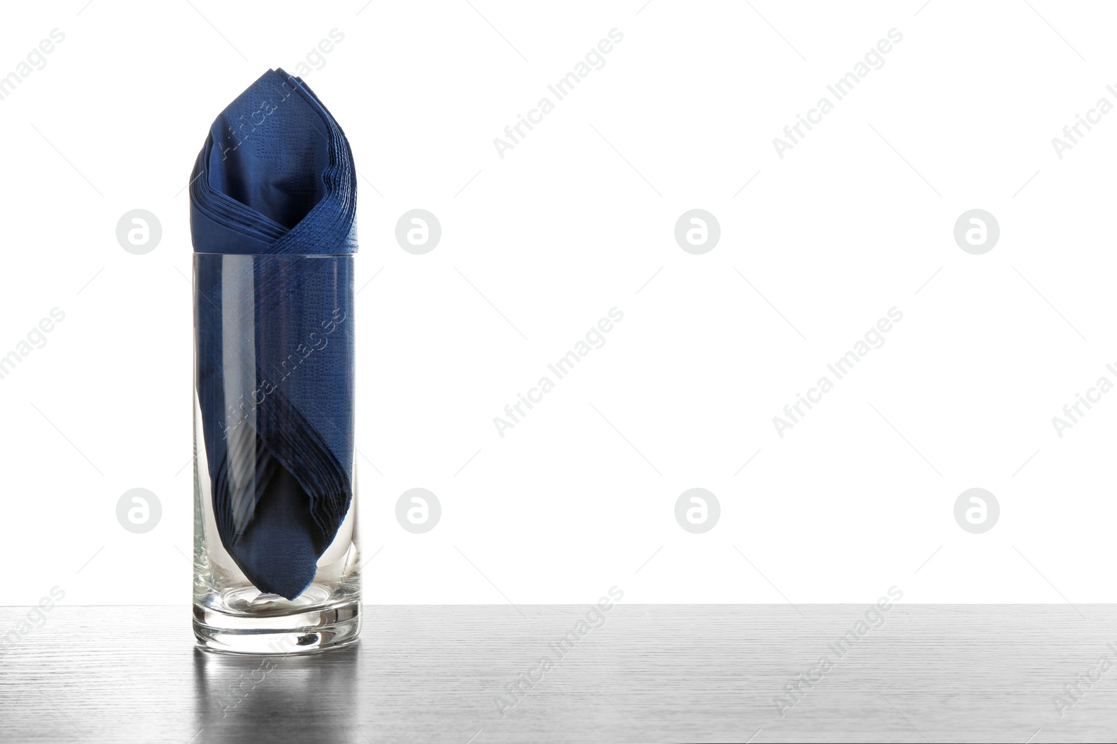 Photo of Glass with paper napkins on table against white background. Space for text