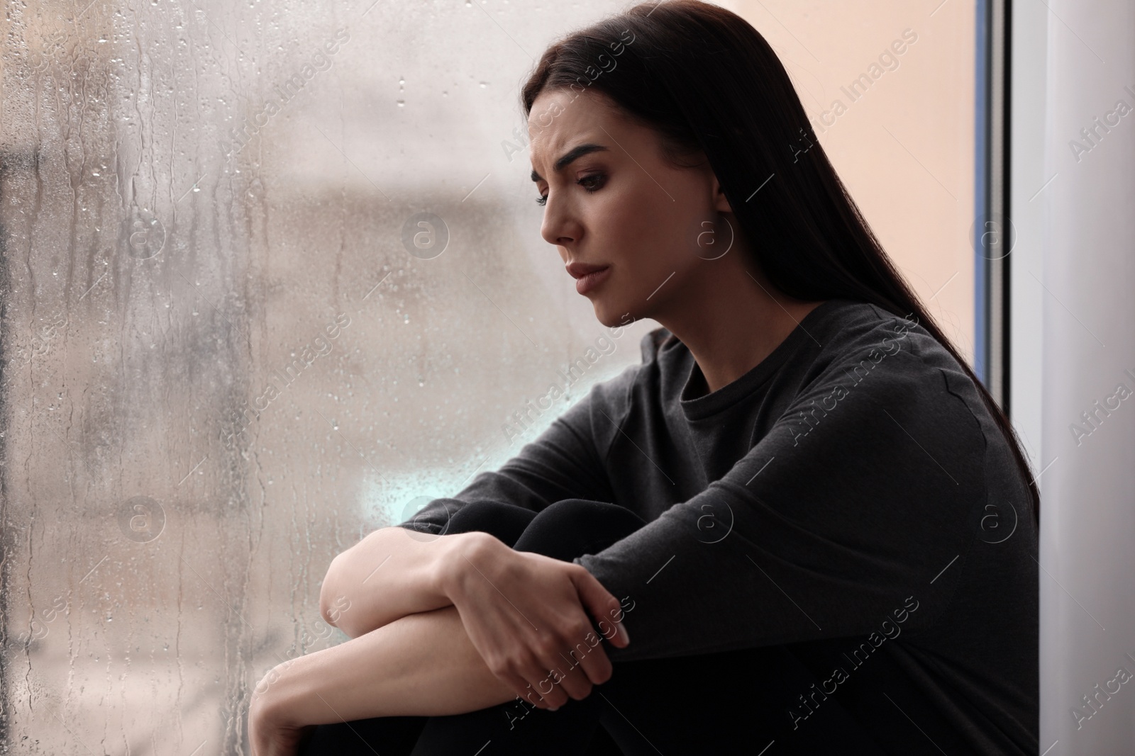 Photo of Depressed woman near window on rainy day, space for text