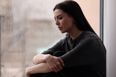 Depressed woman near window on rainy day, space for text