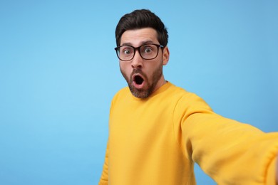 Surprised man taking selfie on light blue background, space for text