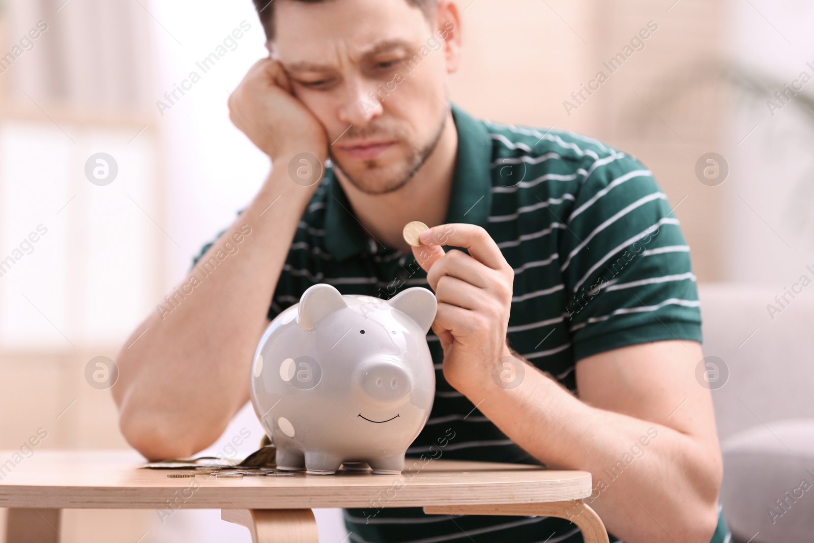 Photo of Sad man with piggy bank and money at home