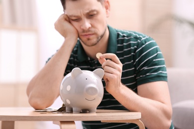 Sad man with piggy bank and money at home