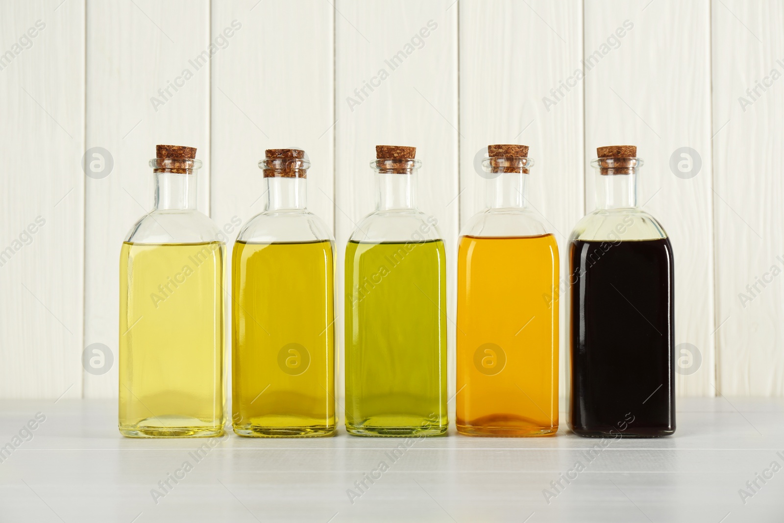 Photo of Vegetable fats. Different cooking oils in glass bottles on white wooden table