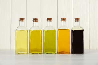 Photo of Vegetable fats. Different cooking oils in glass bottles on white wooden table