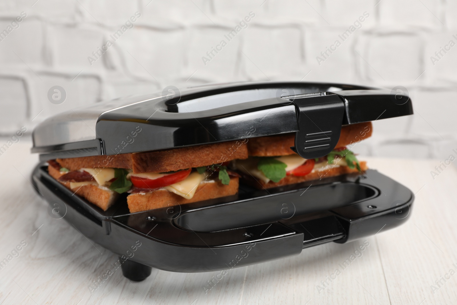 Photo of Modern grill maker with tasty sandwiches on white wooden table, closeup view