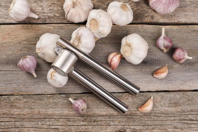 Photo of Garlic press and bulbs on wooden table, flat lay