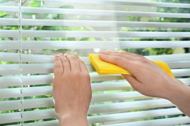 Woman cleaning window blinds with rag indoors, closeup